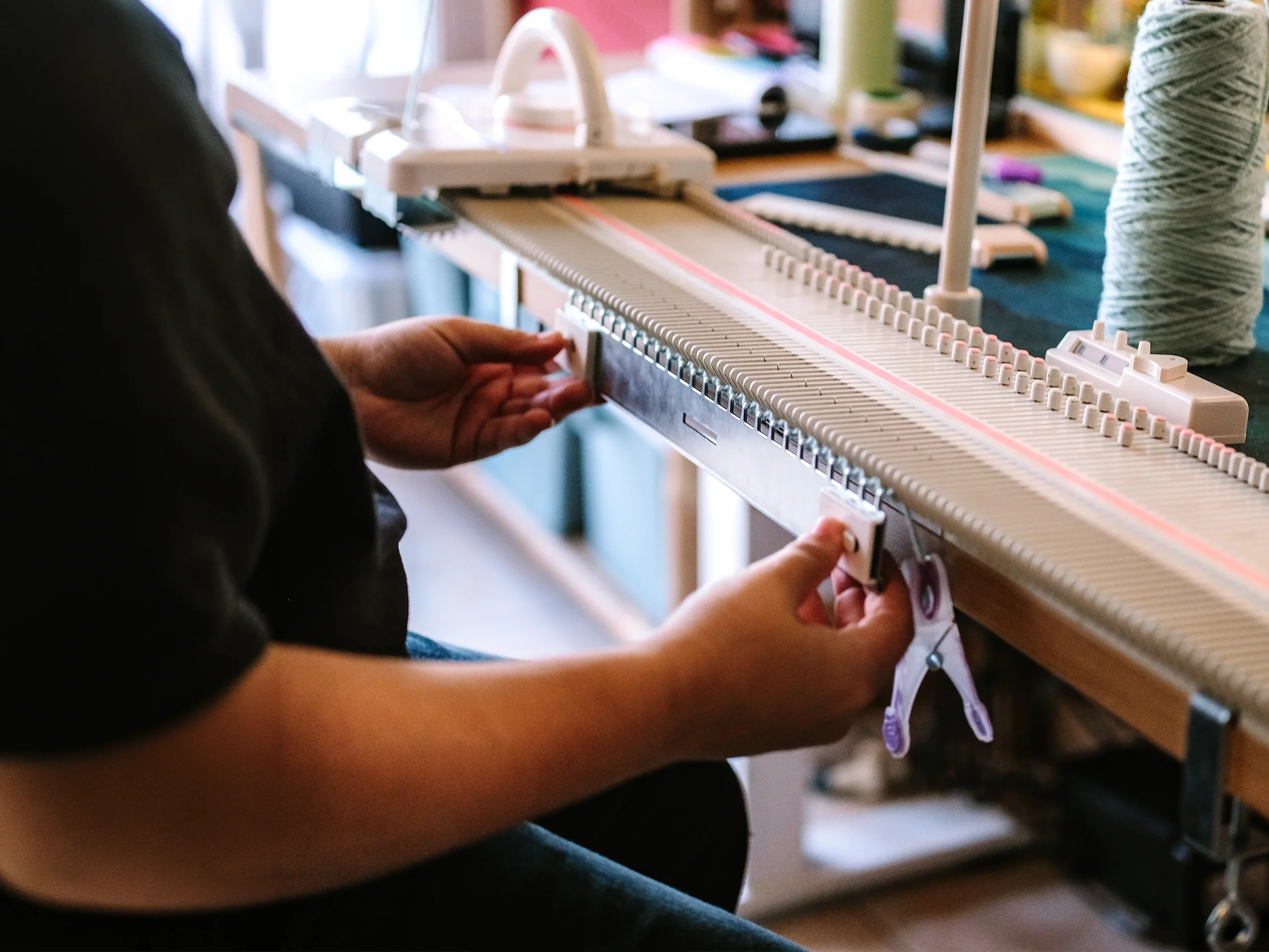 Mains de Maë‑Li sur le métier à tricoter manuel de l'atelier Procyon, bobine de fil vert d'eau