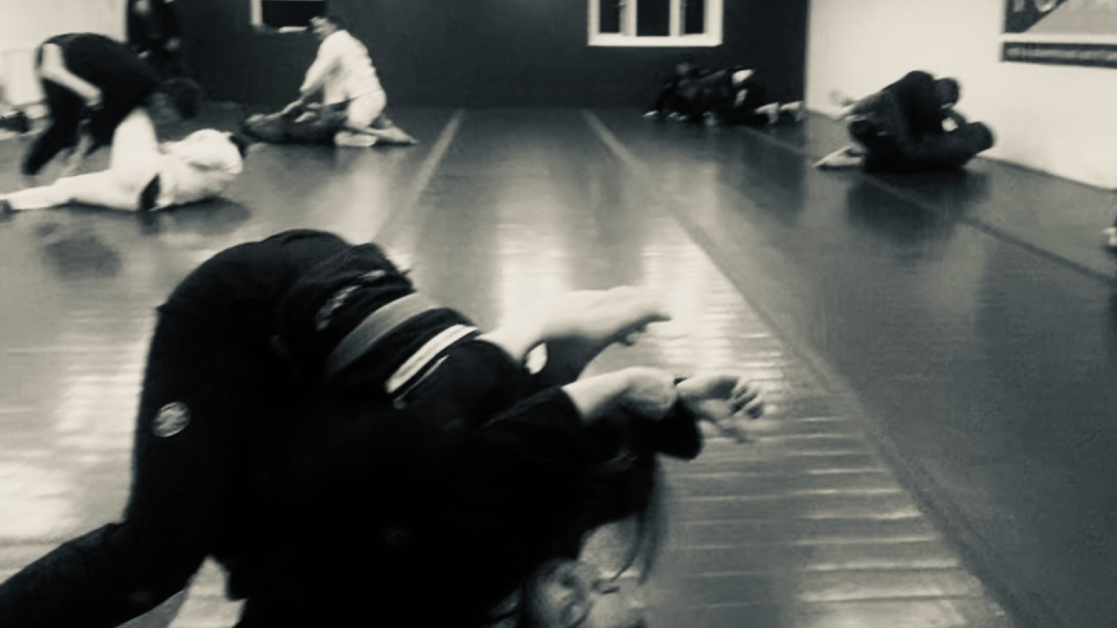 A jiu-jitsu practitioner sitting alone at the edge of the mat tying their white belt in a quiet, dimly lit gym.