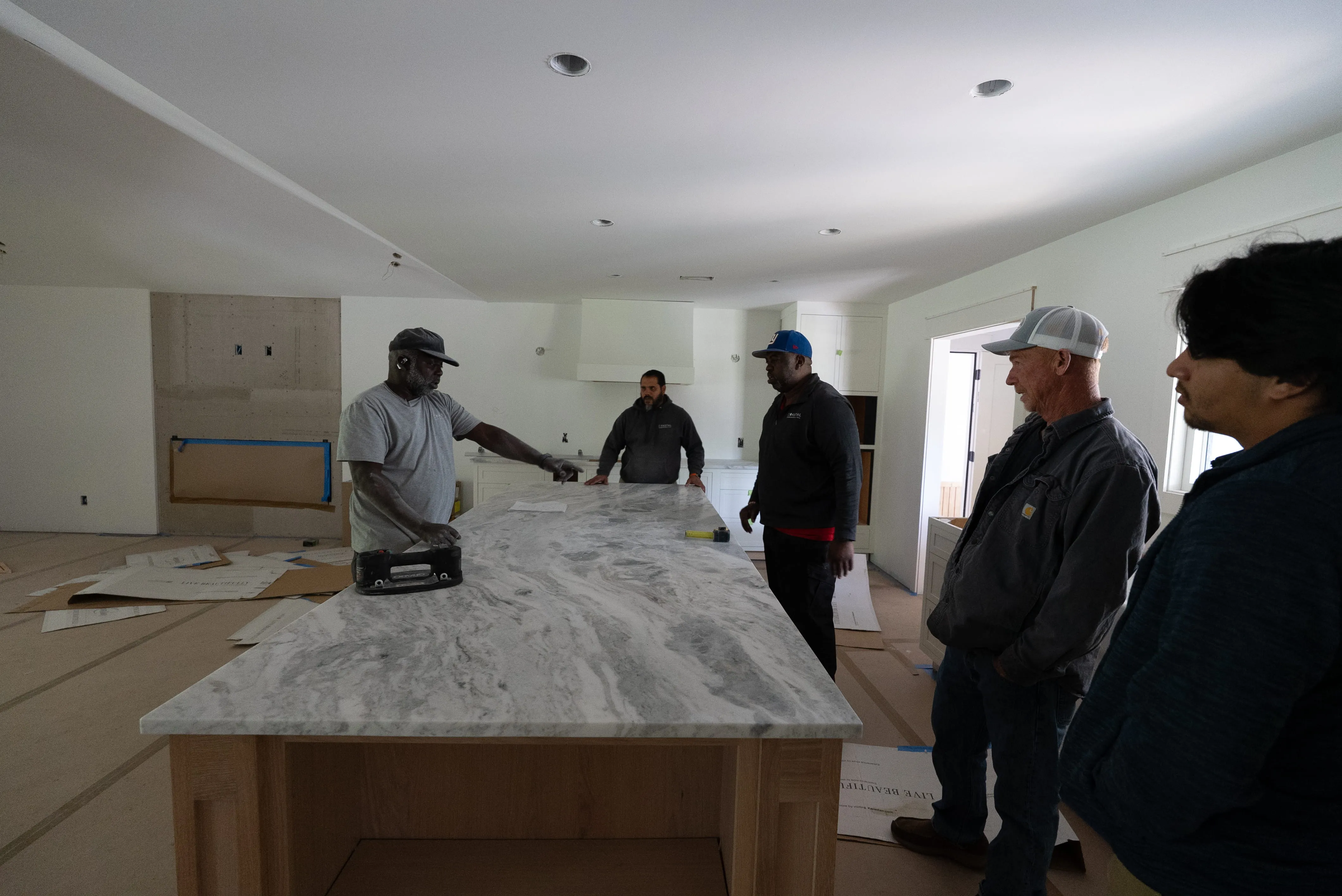 Five men discussing over a large marble kitchen island in an unfinished modern kitchen.