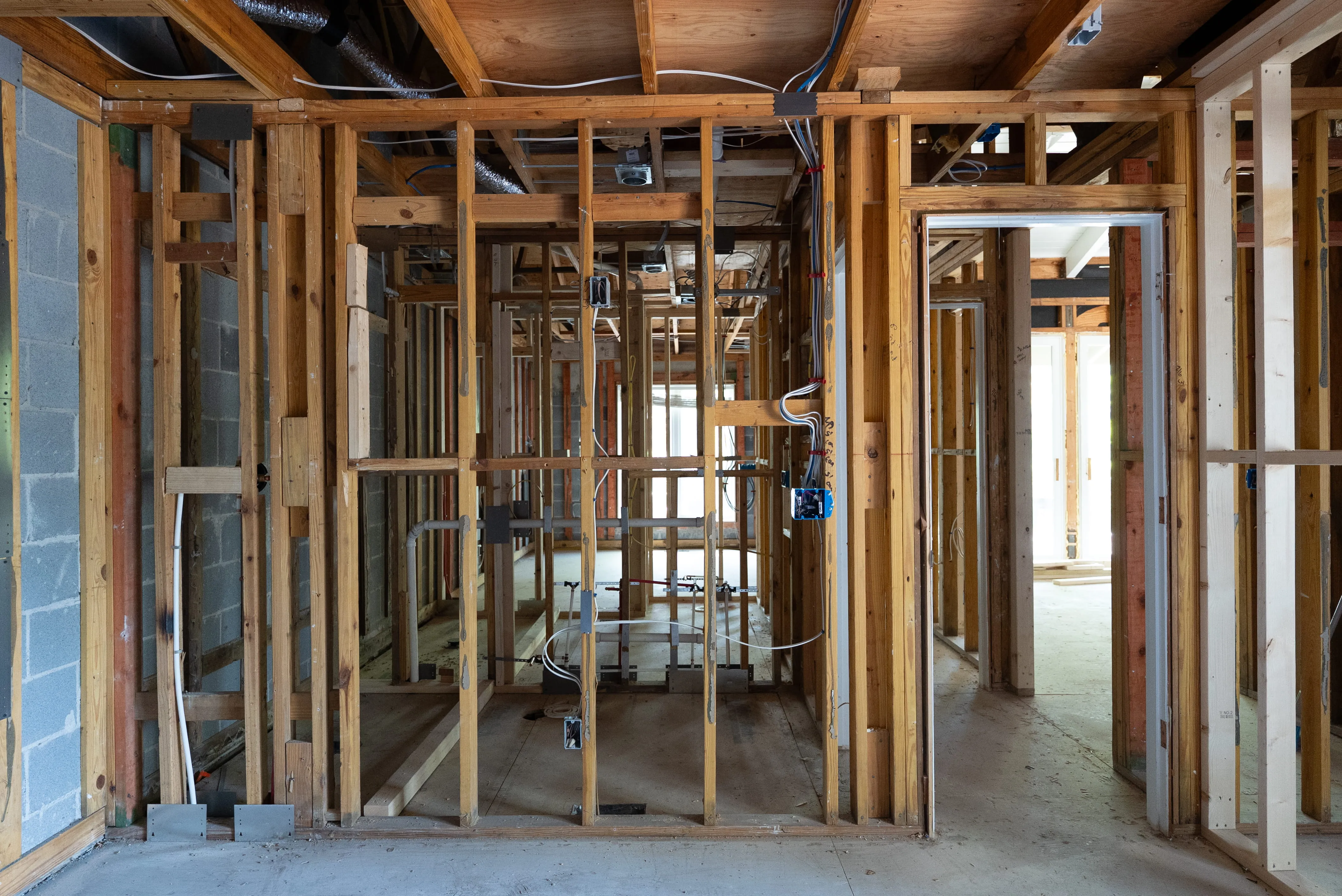 Interior view of a residential building under construction with exposed wooden framing and wiring.