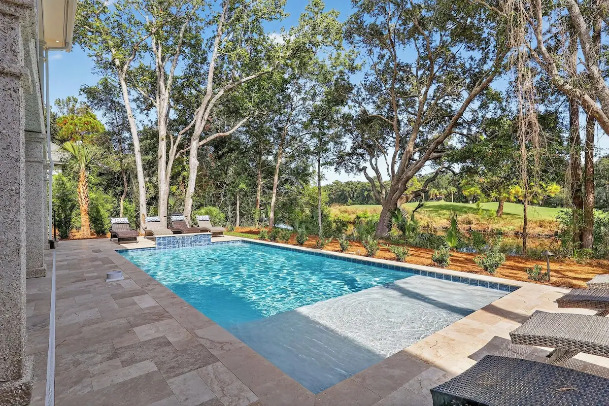 Outdoor rectangular swimming pool with lounge chairs surrounded by trees and greenery.