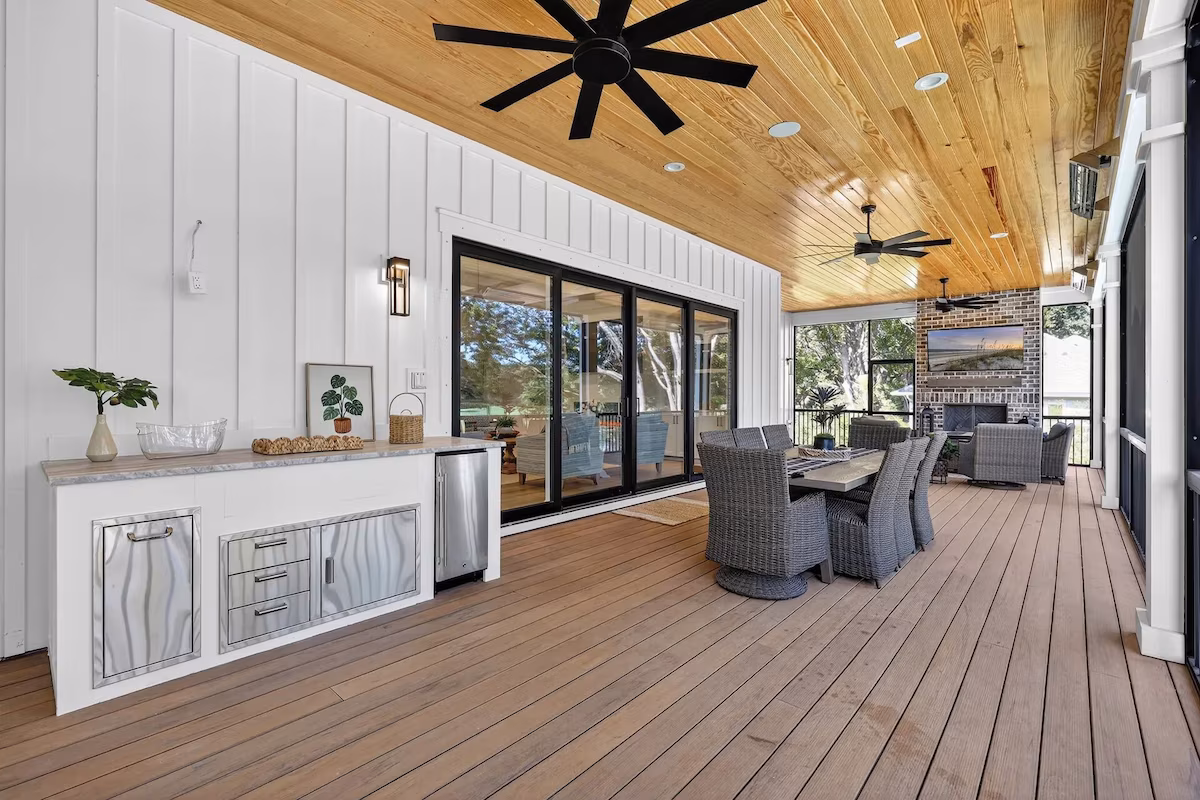 Spacious covered patio with wooden ceiling, dining table, wicker chairs, ceiling fans, and outdoor fireplace.