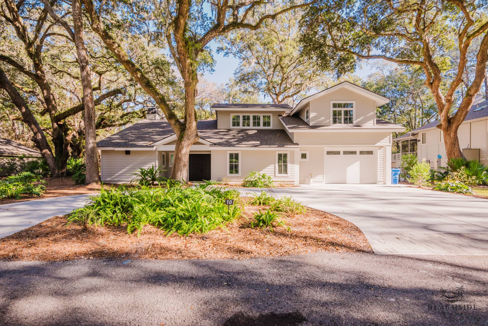 Modern two-story house with a light gray exterior, surrounded by large trees and greenery.