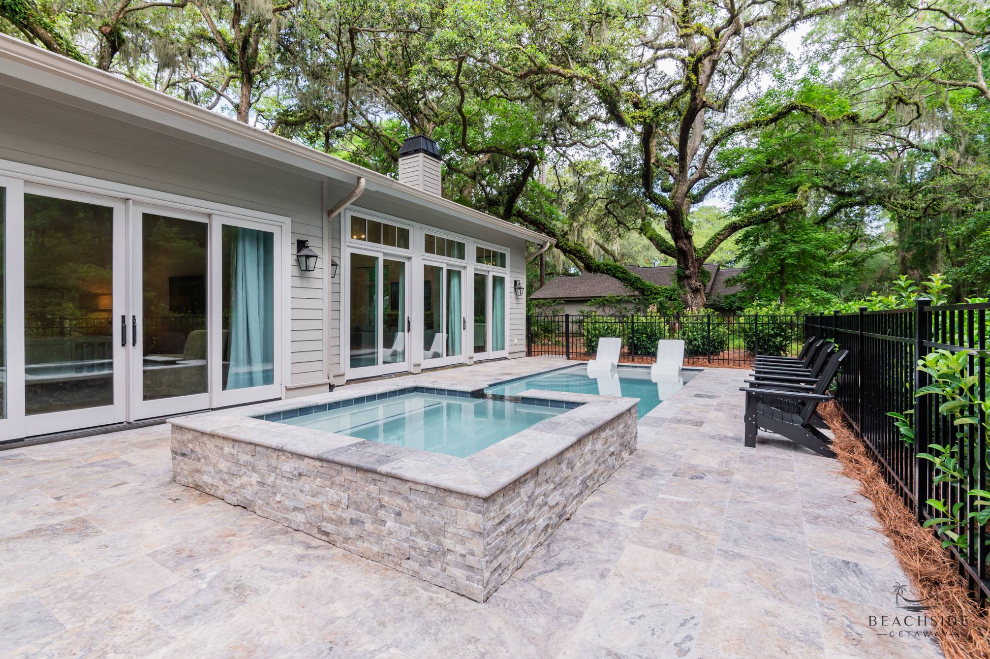 Modern backyard patio with stone hot tub, pool with lounge chairs, and large sliding glass doors.