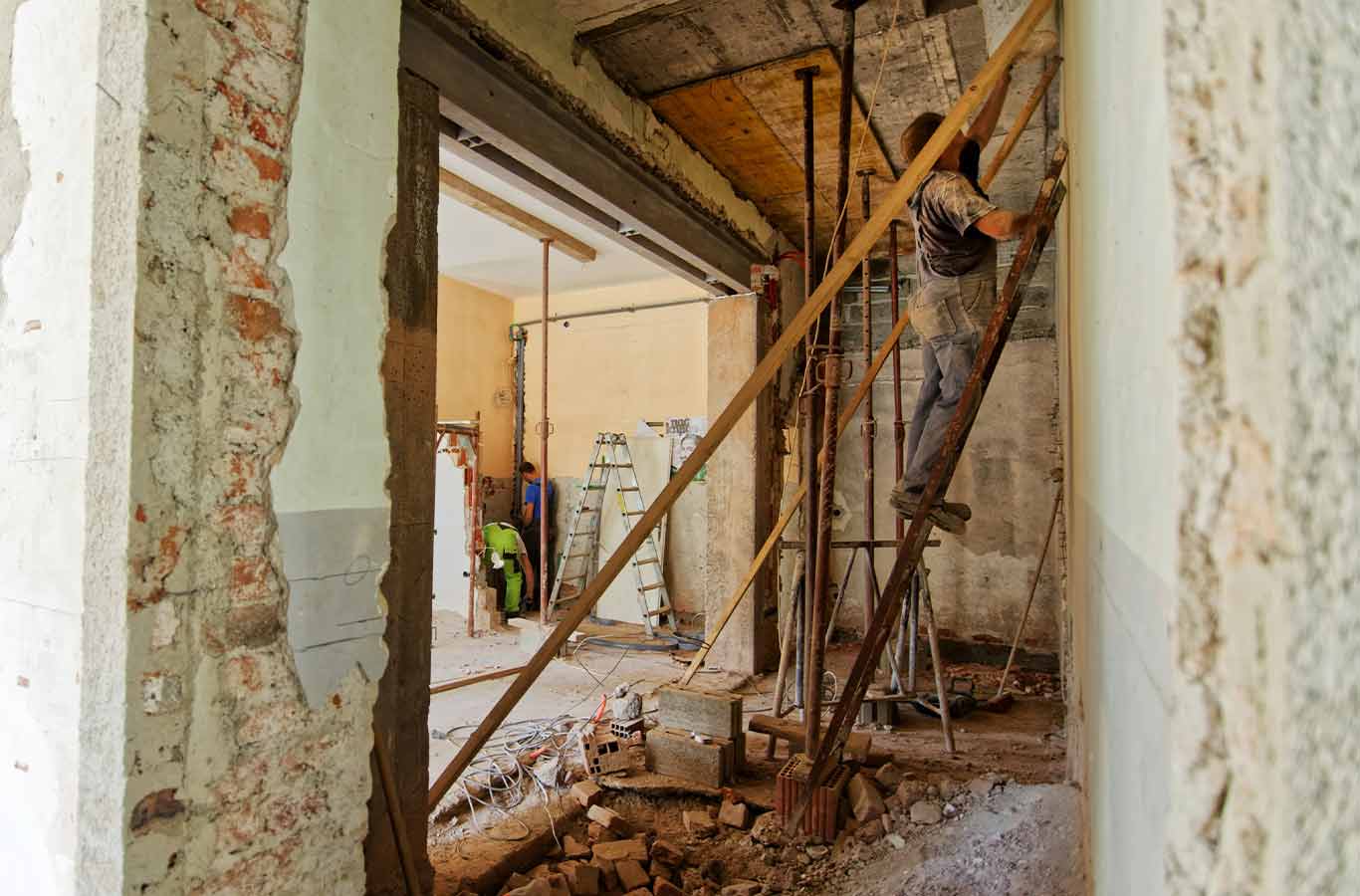 Construction workers renovating an interior space with exposed brick walls and scaffolding.