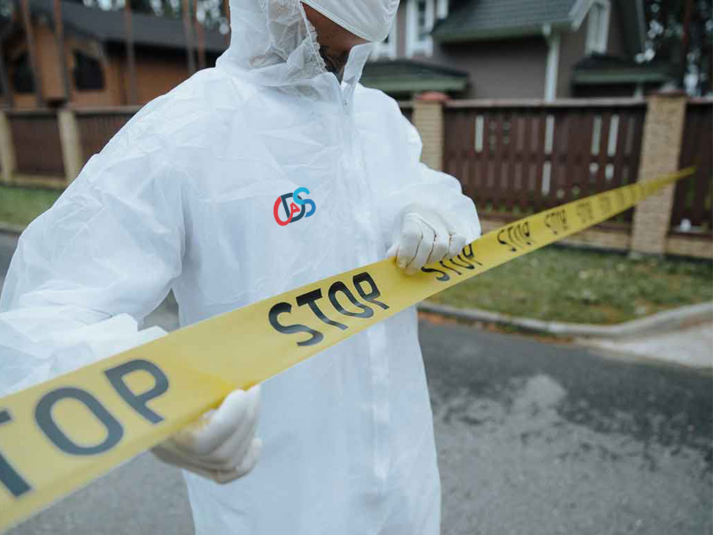 Person in white protective suit holding yellow caution tape with STOP text outside house.