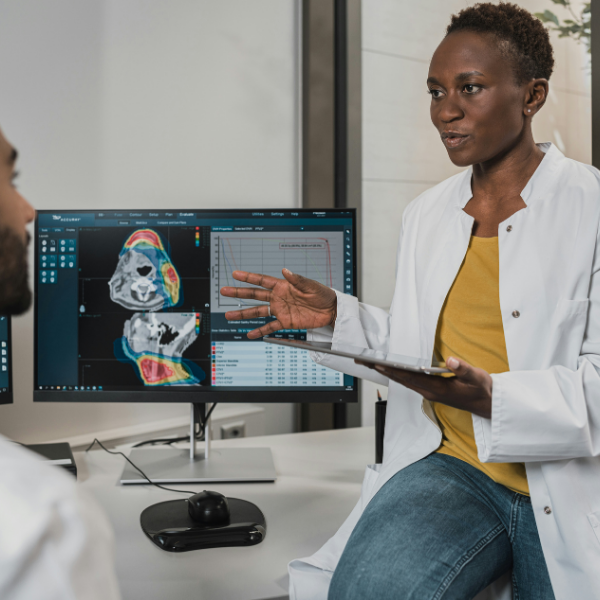 Female doctor explaining medical scans on a monitor to male colleague in a clinical setting.