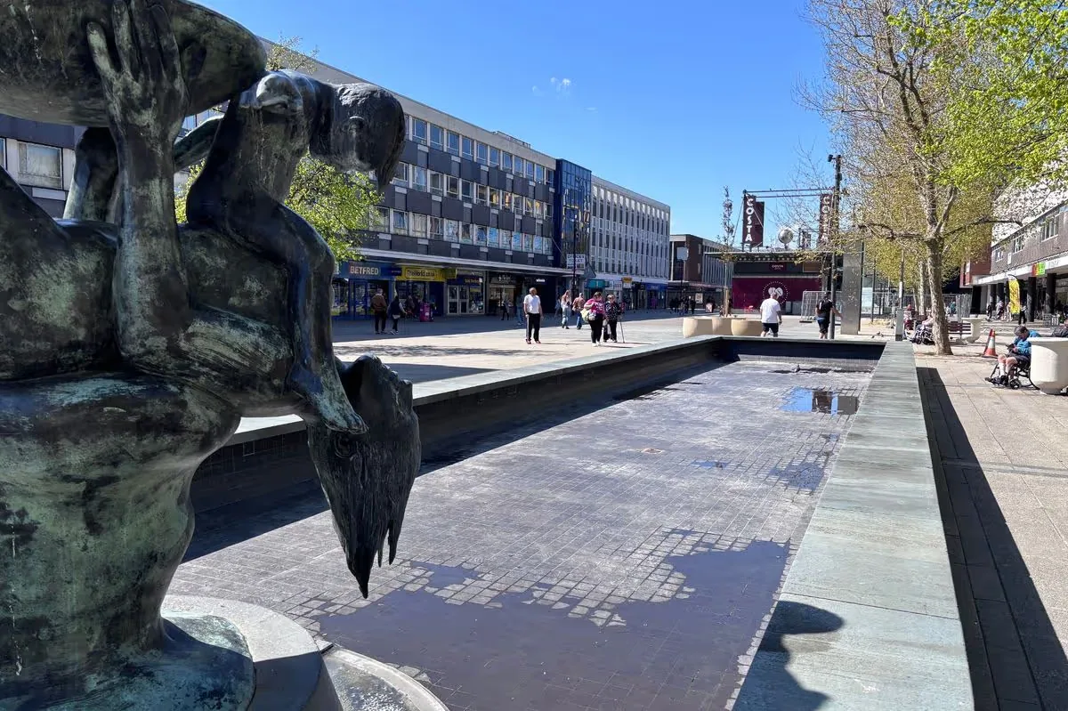 Mother and Child bronze sculpture beside the pool in Basildon Town Square, with shops behind