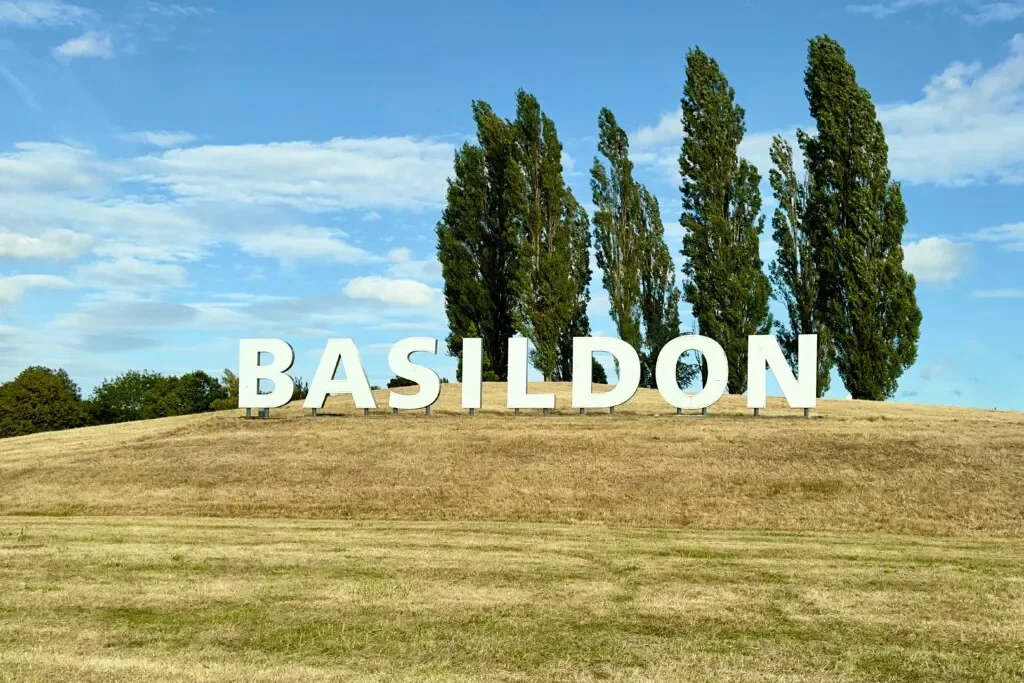 White BASILDON letters on a grassy hill with a row of tall poplar trees behind