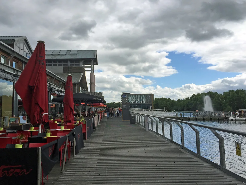 Waterside boardwalk with restaurant seating and a fountain in the lake at Lakeside