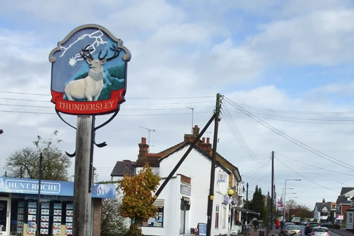Thundersley village sign showing a white stag, beside the road through the village