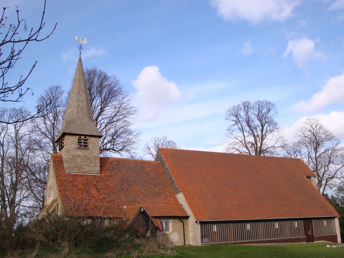 Shingled spire and red tiled roof of St Peter's Church, Thundersley, against a blue sky