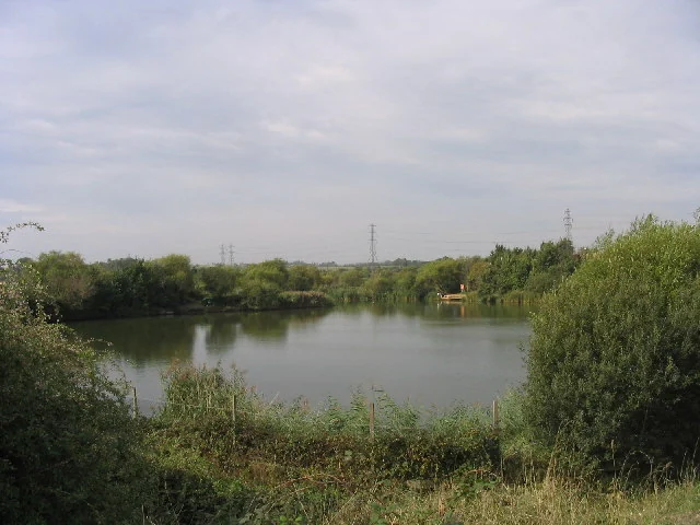 Lake edged with reeds and trees near Stanford-le-Hope under a cloudy sky