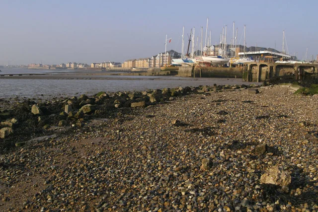 Shingle foreshore on the Thames at Grays with the riverside flats and moored boats beyond