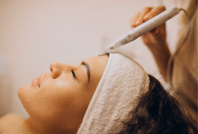 Woman receiving a facial treatment with a handheld device on her forehead, wearing a white headband.