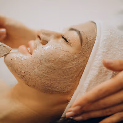 Woman with eyes closed and a facial mask applied, receiving a spa treatment with a towel wrapped around her head.