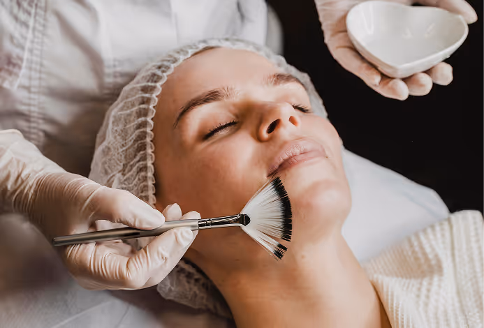 A woman receiving a facial treatment with a fan brush applied to her chin by a person wearing gloves.