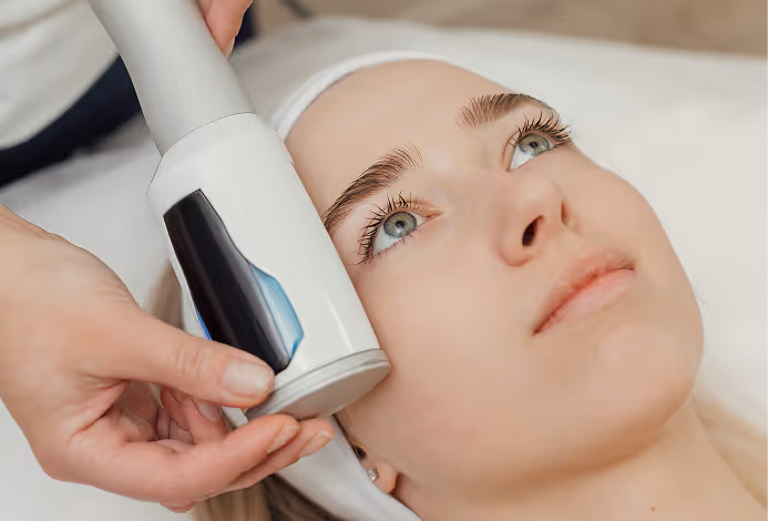 Close-up of a woman receiving a facial treatment with a handheld skin care device on her cheek.