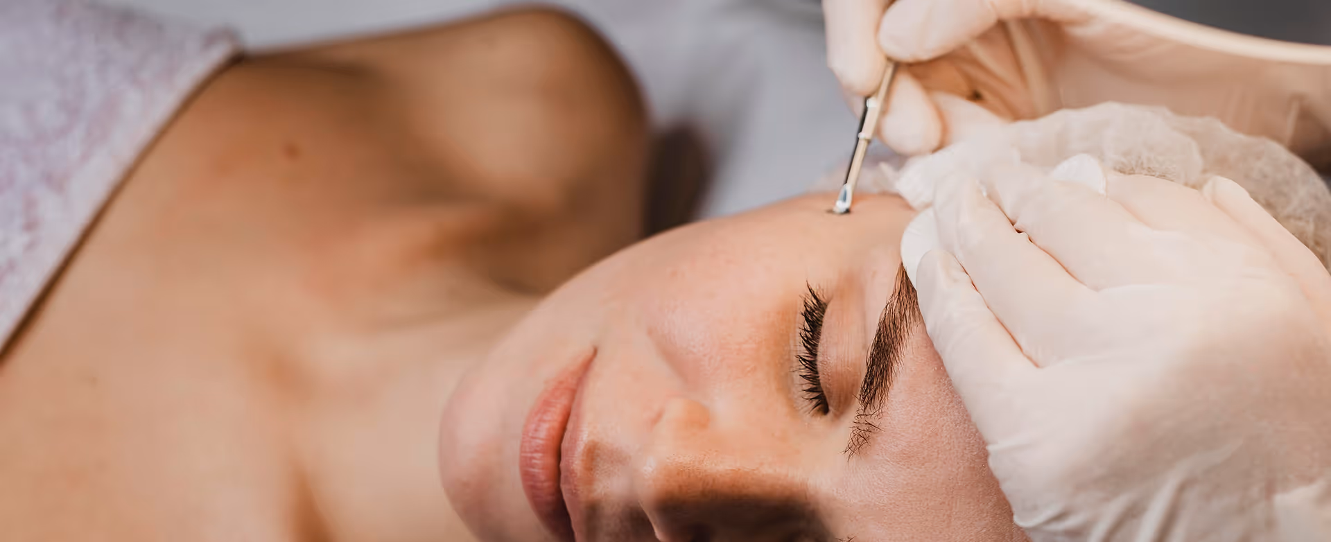 Close-up of a woman receiving a facial extraction treatment with a metal tool by a gloved professional.