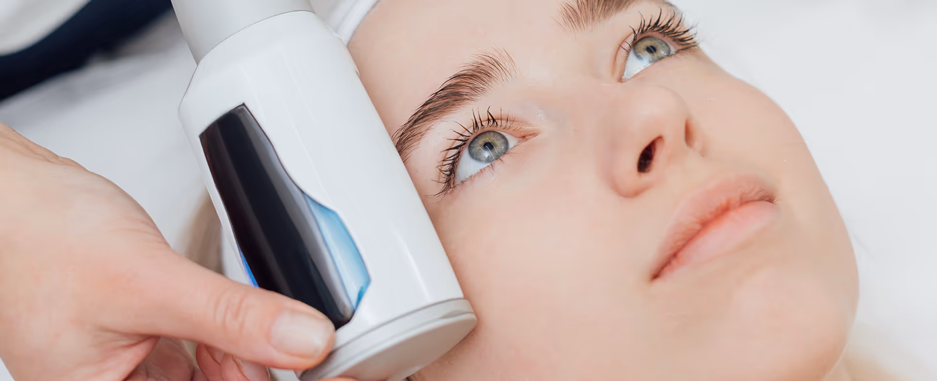 Close-up of a woman receiving a facial treatment with a handheld skincare device near her cheek.