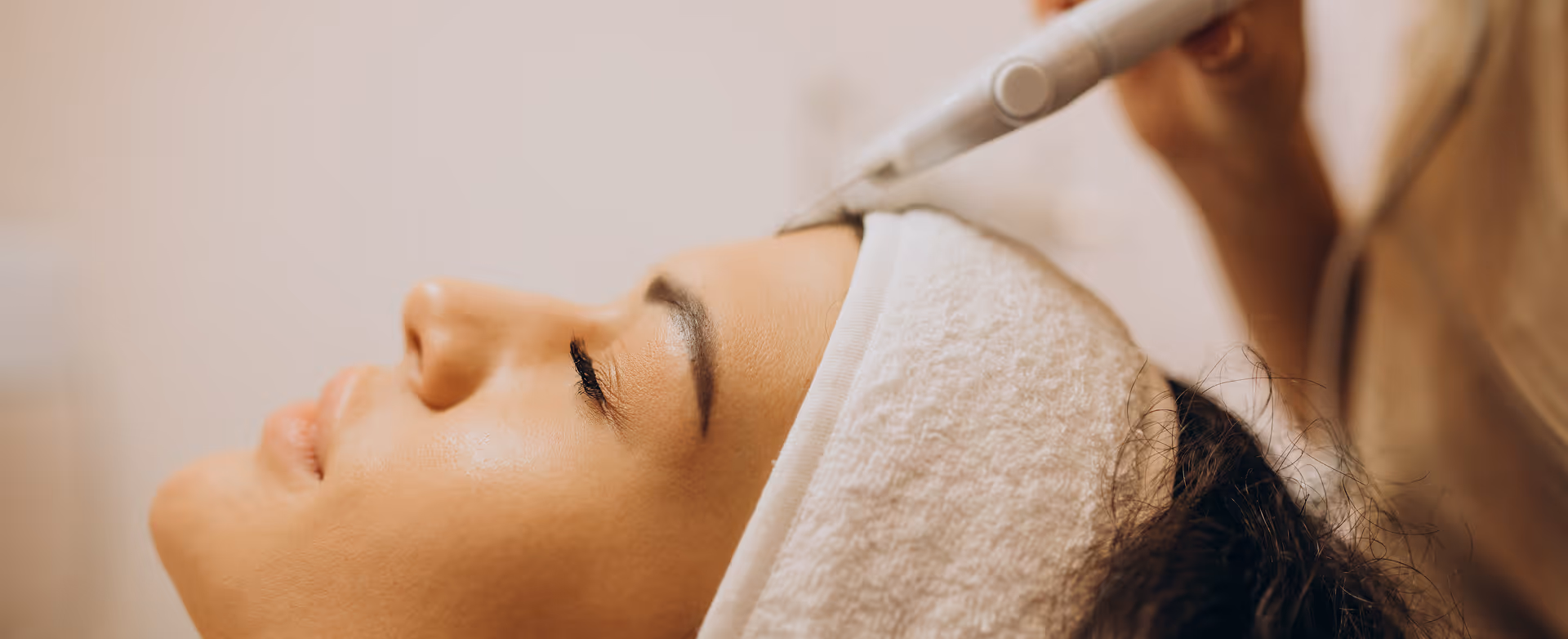 Close-up of a woman with eyes closed receiving a facial treatment with a handheld device at a spa.