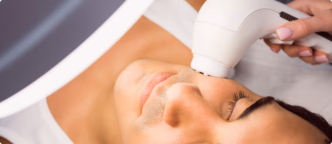 Close-up of a man receiving a facial treatment with a white handheld device on his cheek.