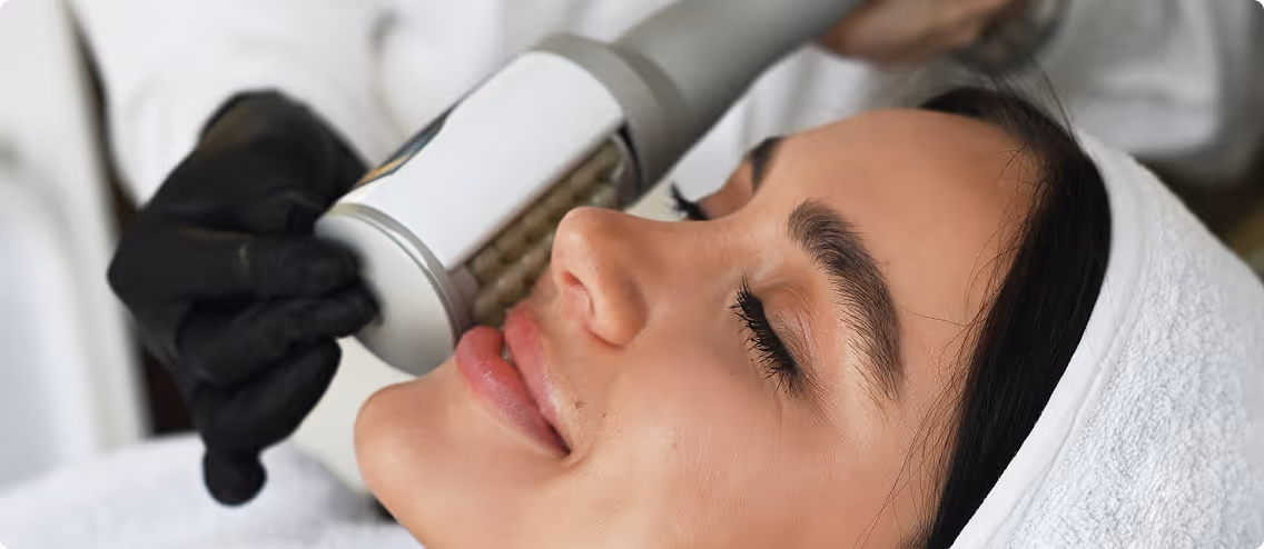 Woman receiving a facial treatment with a handheld device by a gloved practitioner.