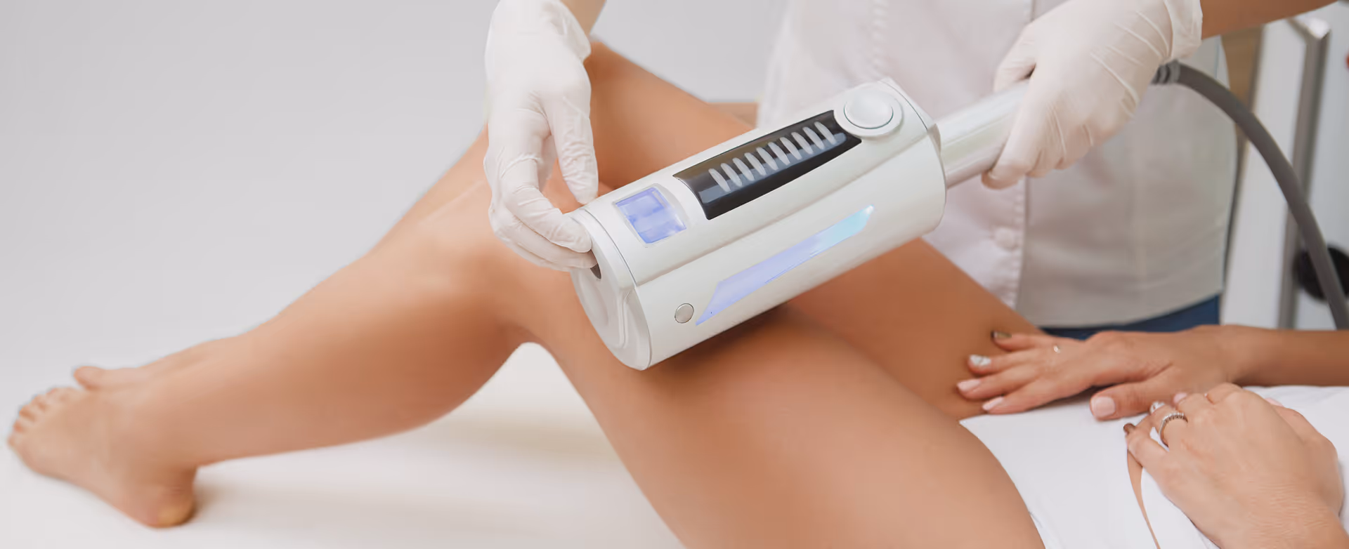 Close-up of a professional wearing gloves performing a laser hair removal treatment on a woman's thigh using a handheld device.