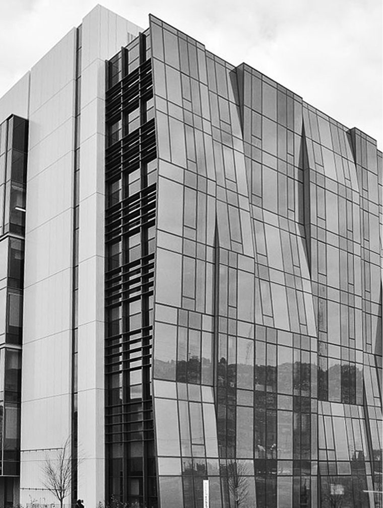 Modern multi-story building with a reflective glass facade and a white concrete section on the side.