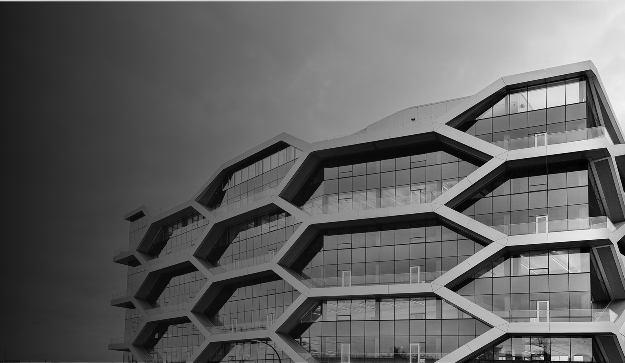 Modern building facade with hexagonal white frames and large glass windows against a cloudy sky.
