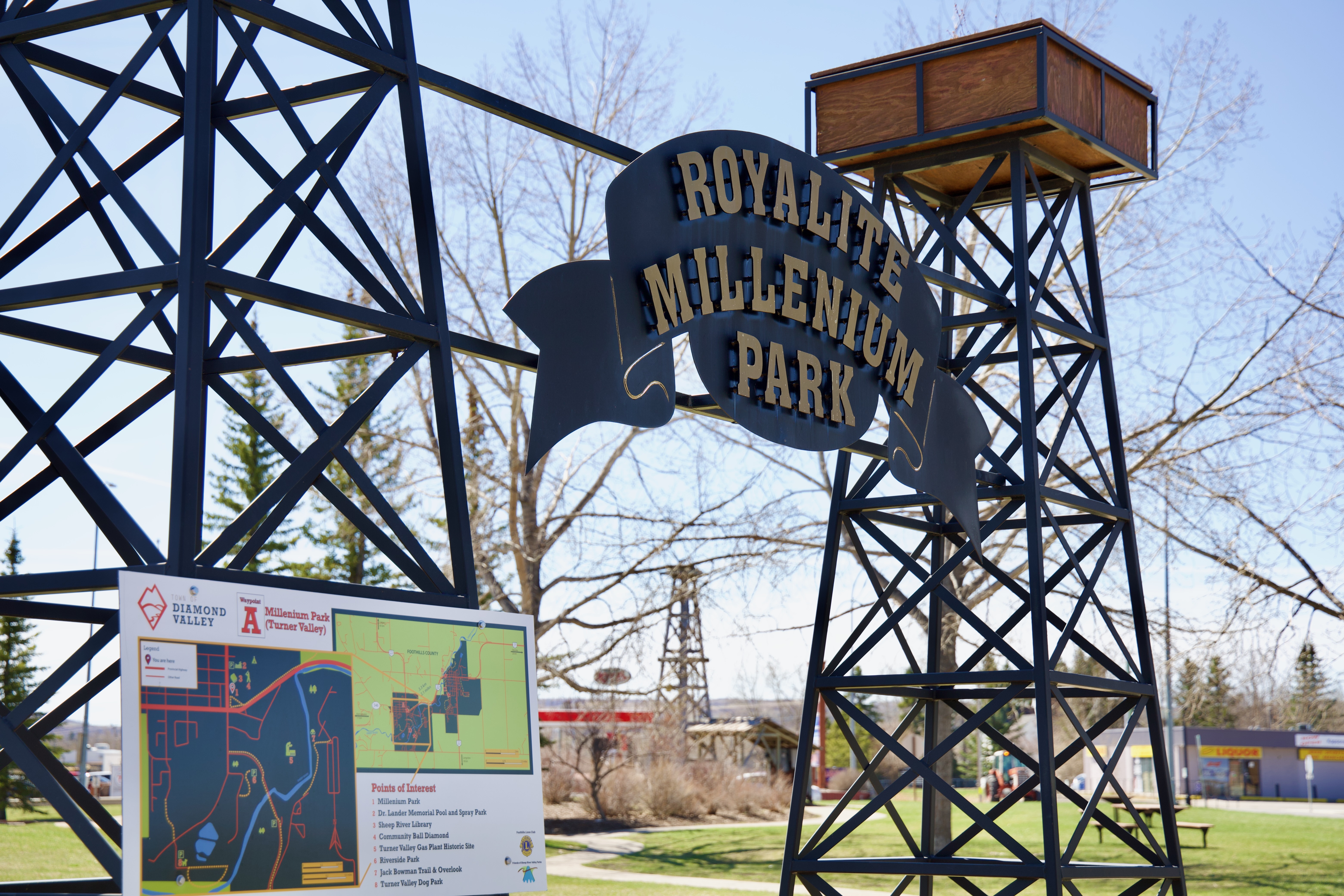 Black metal park entrance structure with sign reading Royalite Millennium Park and a nearby map board.