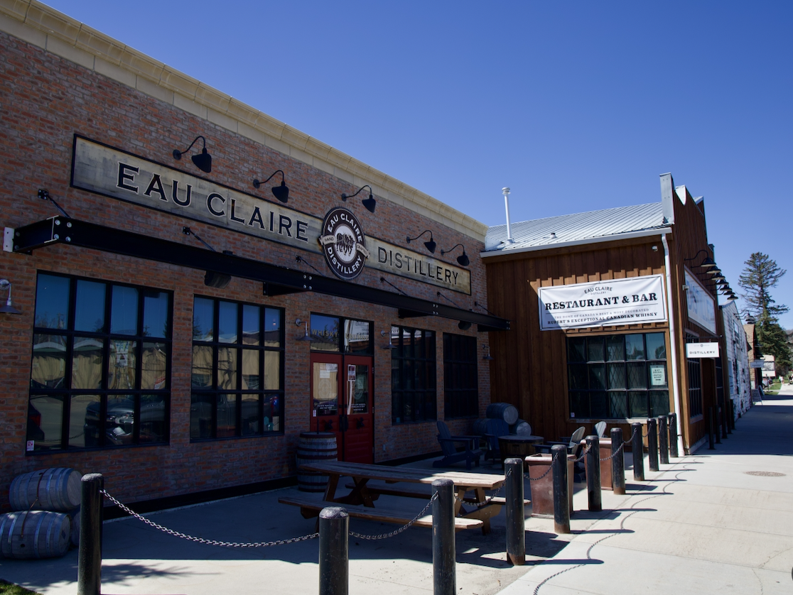 Eau Claire Distillery building with outdoor seating and banners for restaurant and bar under blue sky.