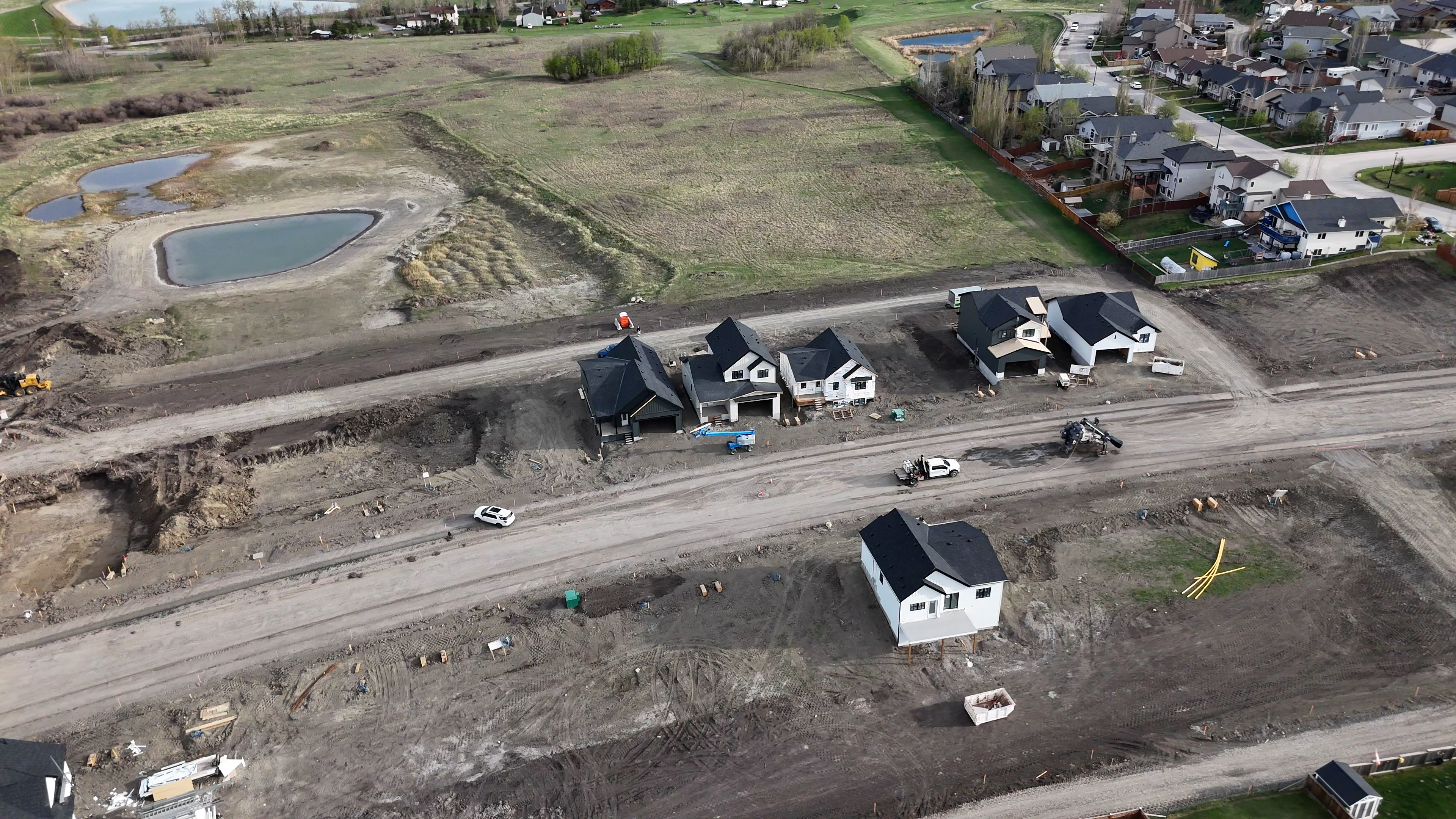 Aerial view of new houses under construction with dirt roads and nearby completed residential area.
