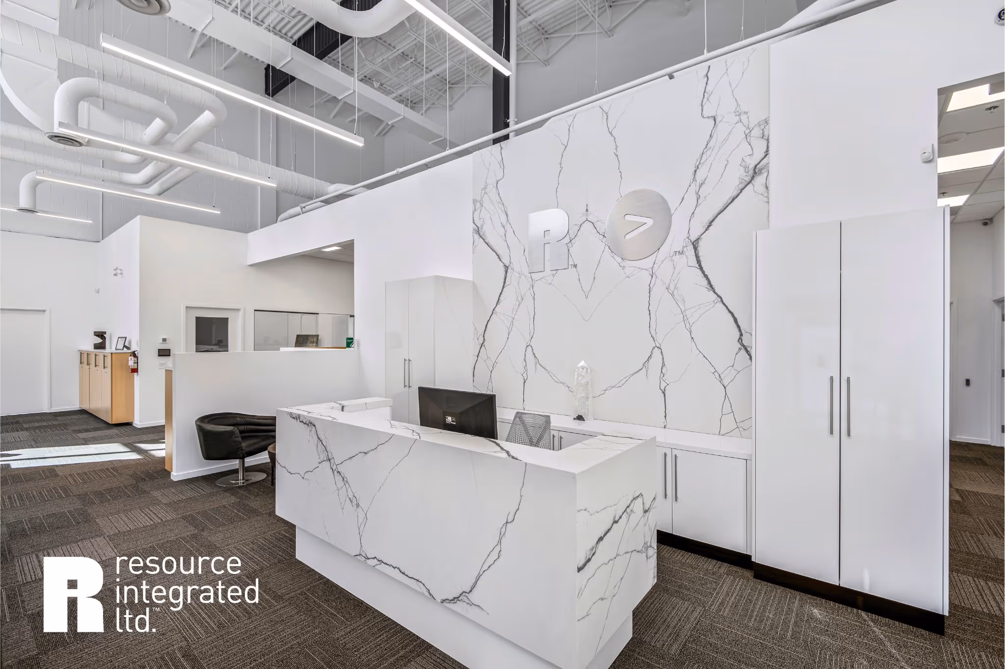 Modern office reception area with marble-patterned front desk, white storage cabinets, and Resource Integrated Ltd. logo on the wall.