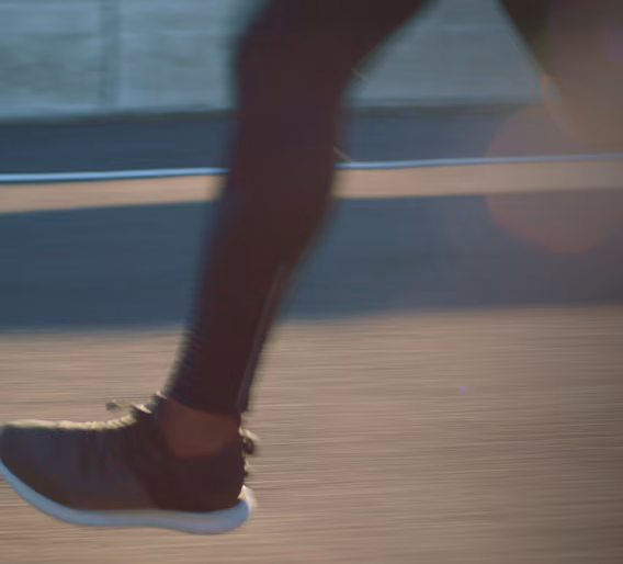 Close-up of a person's black running shoe in motion on a paved surface near a waterfront.