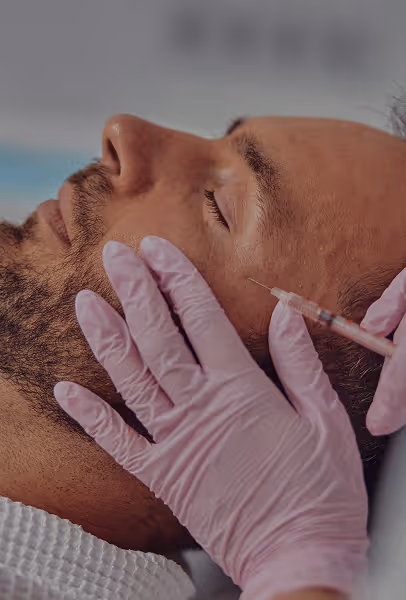 Man receiving an injection in the temple area of his face, administered by a person wearing pink gloves.