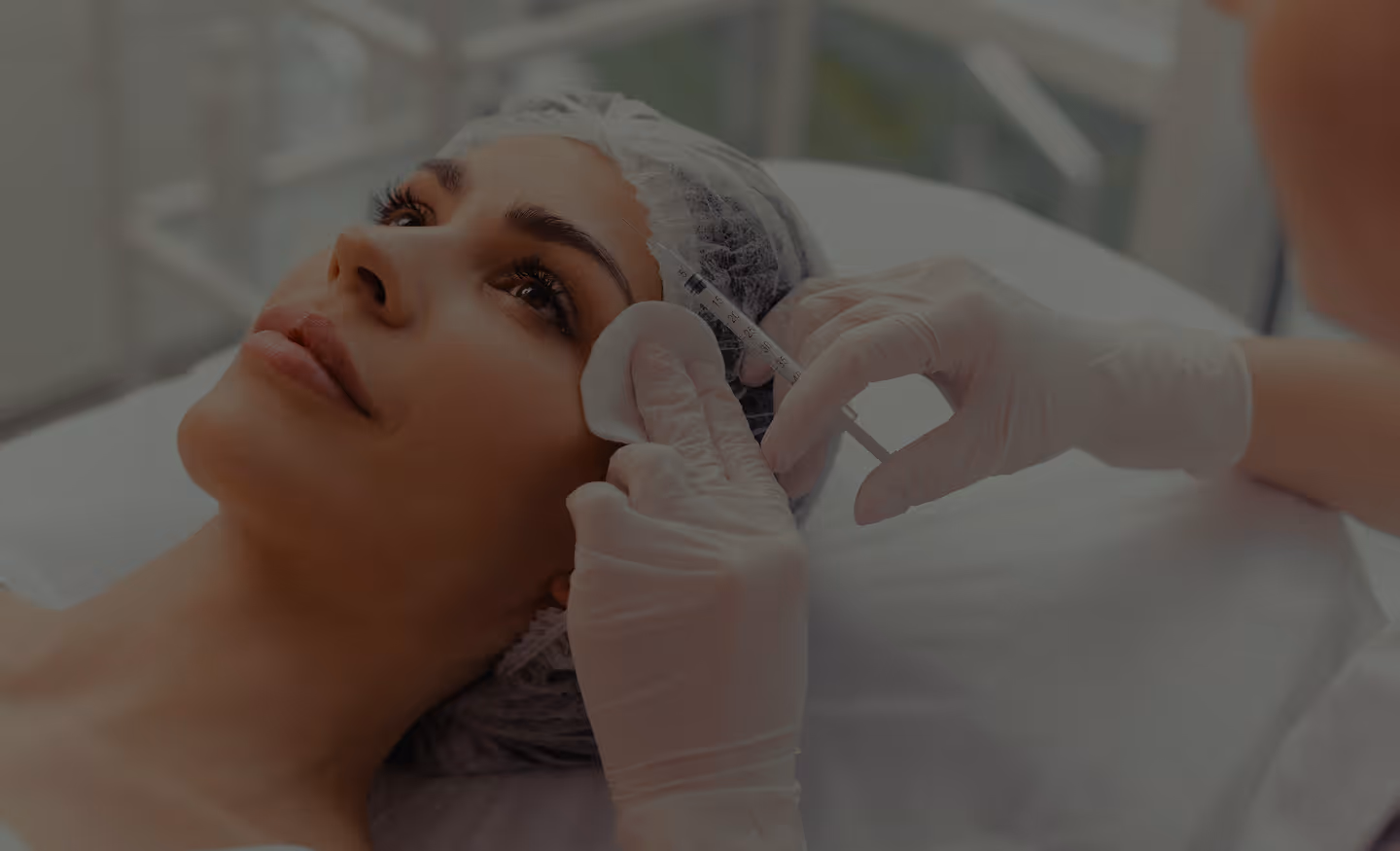 Woman receiving a cosmetic injection near her temple from a gloved medical professional.