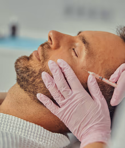 Man receiving a cosmetic facial injection from a gloved professional.
