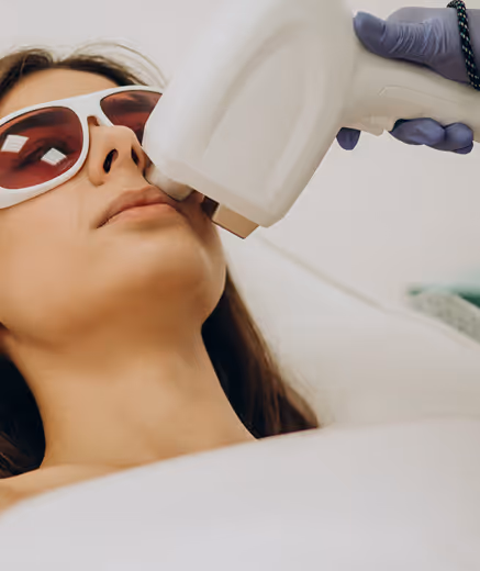 Woman wearing protective eyewear receiving laser treatment on her upper lip from a gloved technician.