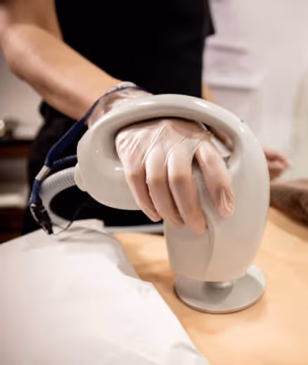 Person wearing gloves using a handheld white device on a person's back, likely for a skin or body treatment.