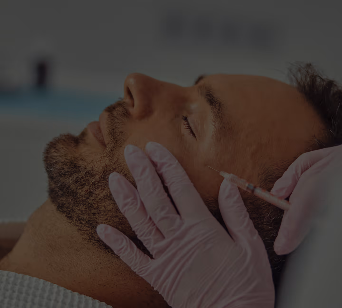 Close-up of a man with eyes closed receiving a cosmetic injection in the cheek administered by a person wearing pink gloves.