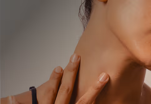 Close-up of a person touching their neck with fingers, showcasing smooth skin and a neutral background.