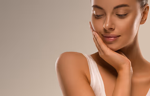 Close-up of a woman gently touching her face with eyes closed and a serene expression.
