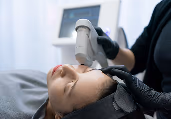 Patient receiving a facial treatment with a handheld device by a professional wearing black gloves.