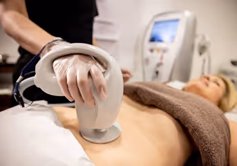 Close-up of a person receiving a body contouring or ultrasound treatment on the abdomen with a handheld device.