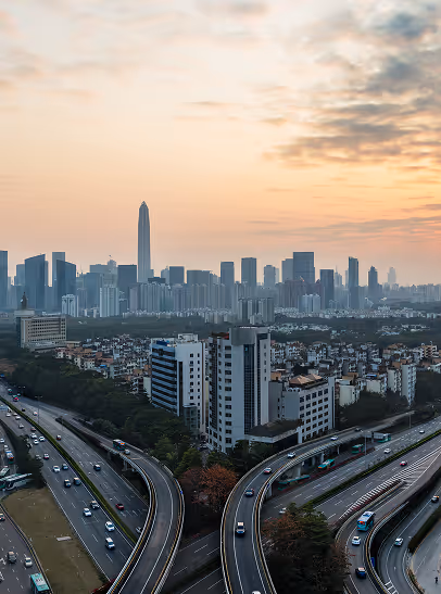 Aerial view of a city skyline at sunset with tall buildings and curved highways filled with cars.