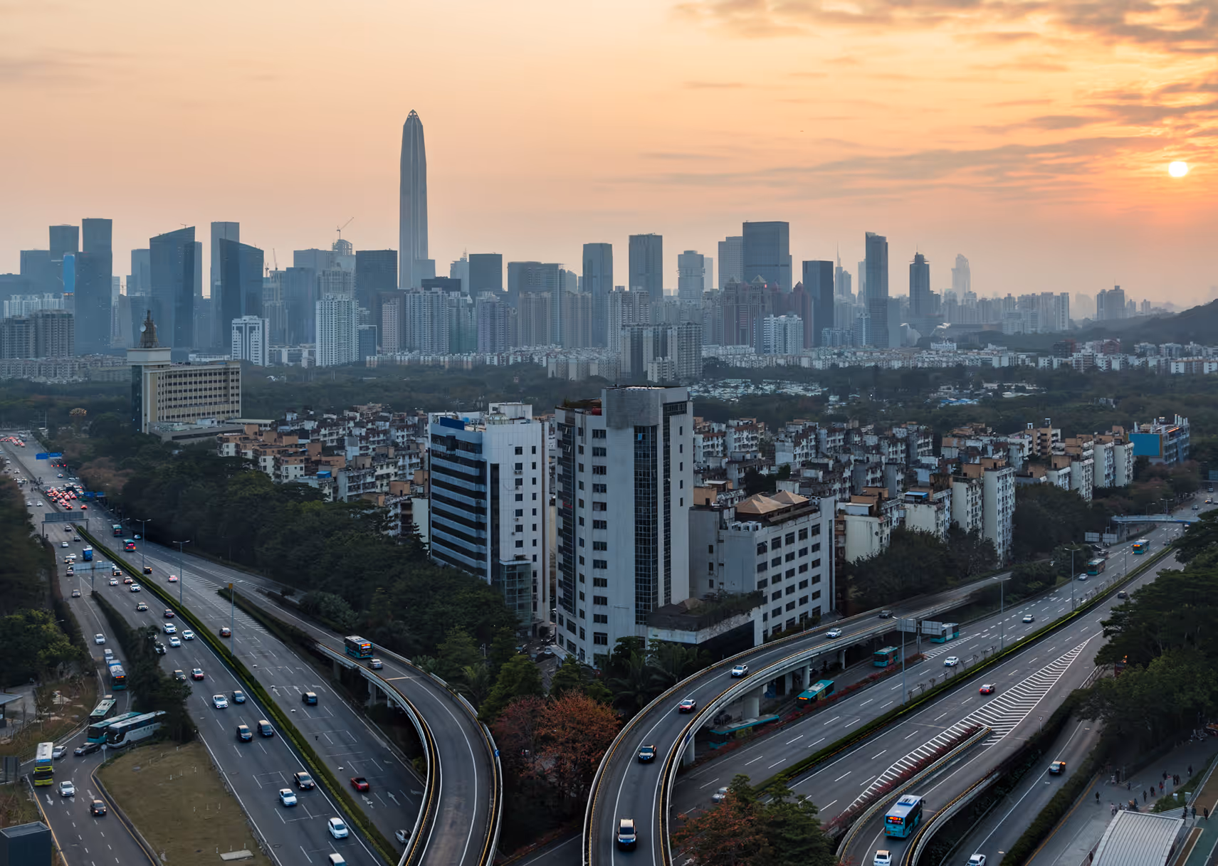 Urban cityscape with highways curving around buildings and a skyline of skyscrapers at sunset.