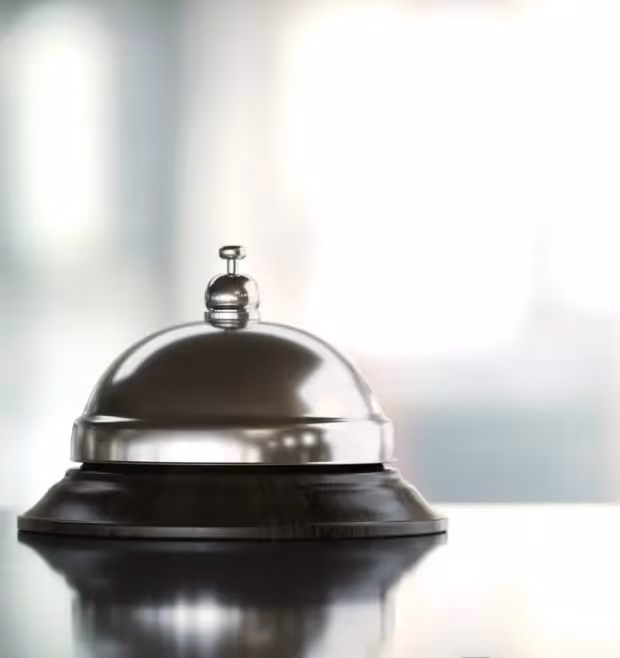 Shiny metal service bell on a reflective surface with a blurred background.