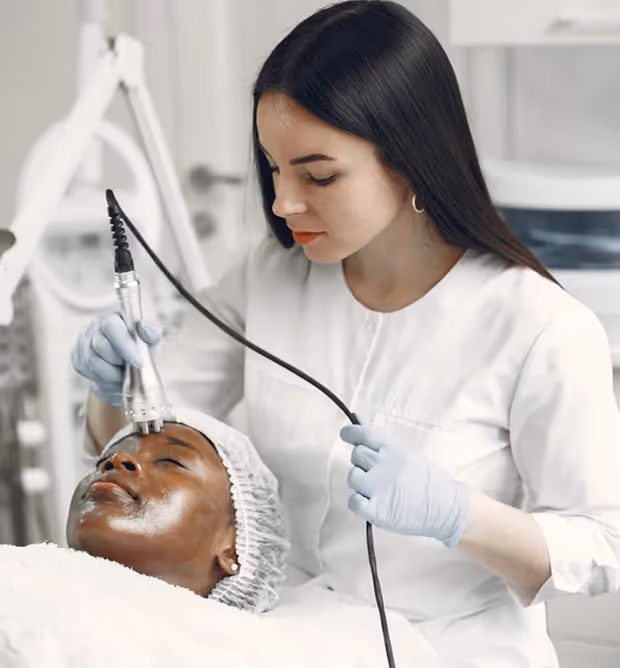 Esthetician wearing gloves performing a facial treatment with a handheld device on a client lying down with a headband.