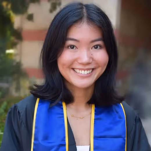 Young woman with shoulder-length black hair wearing a blue and yellow graduation stole smiling outdoors.